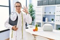 Young hispanic woman as nutritionist doctor holding weighing machine doing ok sign with fingers, smiling friendly gesturing