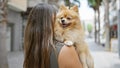 Young hispanic woman, captured from the back standing on a sunny city street, while backwards hugging her beautiful dog, embodying Royalty Free Stock Photo