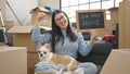 Young hispanic woman with chihuahua dog smiling confident holding blackboard and keys at new home Royalty Free Stock Photo