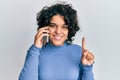 Young hispanic woman with curly hair having conversation talking on the smartphone smiling with an idea or question pointing Royalty Free Stock Photo