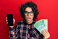 Young hispanic woman with curly hair showing smartphone screen holding 200 ruble afraid and shocked with surprise and amazed Royalty Free Stock Photo