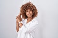 Young hispanic woman with curly hair standing over white background holding symbolic gun with hand gesture, playing killing