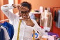 Young hispanic woman with curly hair standing at tailor room smiling making frame with hands and fingers with happy face