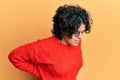 Young hispanic woman with curly hair wearing casual winter sweater suffering of backache, touching back with hand, muscular pain Royalty Free Stock Photo