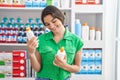 Young hispanic woman customer smiling confident holding lotion bottles at pharmacy Royalty Free Stock Photo