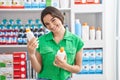 Young hispanic woman customer smiling confident holding lotion bottles at pharmacy Royalty Free Stock Photo