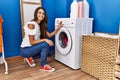 Young hispanic woman doing laundry choosing washing machine program looking positive and happy standing and smiling with a Royalty Free Stock Photo