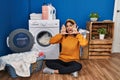 Young hispanic woman doing laundry smiling cheerful playing peek a boo with hands showing face