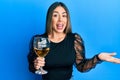 Young hispanic woman drinking a glass of red wine celebrating achievement with happy smile and winner expression with raised hand Royalty Free Stock Photo