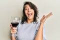 Young hispanic woman drinking a glass of red wine celebrating victory with happy smile and winner expression with raised hands Royalty Free Stock Photo