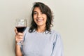 Young hispanic woman drinking a glass of red wine looking positive and happy standing and smiling with a confident smile showing Royalty Free Stock Photo