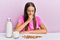 Young hispanic woman drinking healthy almond milk sitting on the table feeling unwell and coughing as symptom for cold or Royalty Free Stock Photo