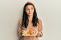 Young hispanic woman eating a tasty classic burger smiling looking to the side and staring away thinking Royalty Free Stock Photo