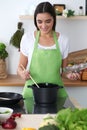 Young Hispanic woman in a green apron cooking in the kitchen. Housewife found a new recipe for her soup.