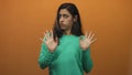 Young hispanic woman with hands raised palms out in studio with orange backdrop and recoiling expression; disgust Royalty Free Stock Photo