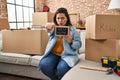 Young hispanic woman holding blackboard with new home text pointing with finger to the camera and to you, confident gesture Royalty Free Stock Photo