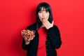 Young hispanic woman holding bowl of chestnuts covering mouth with hand, shocked and afraid for mistake Royalty Free Stock Photo