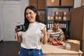 Young hispanic woman holding camera working at small business ecommerce smiling happy and positive, thumb up doing excellent and Royalty Free Stock Photo