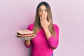 Young hispanic woman holding carrot cake covering mouth with hand, shocked and afraid for mistake Royalty Free Stock Photo