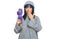 Young hispanic woman holding closed purple umbrella covering mouth with hand, shocked and afraid for mistake