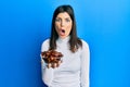 Young hispanic woman holding dates bowl scared and amazed with open mouth for surprise, disbelief face