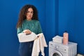 Young hispanic woman holding dirty laundry and detergent bottle depressed and worry for distress, crying angry and afraid Royalty Free Stock Photo