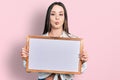 Young hispanic woman holding empty white chalkboard making fish face with mouth and squinting eyes, crazy and comical Royalty Free Stock Photo