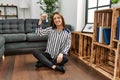 Young hispanic woman holding key of new house sitting on floor at home Royalty Free Stock Photo