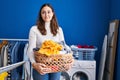 Young hispanic woman holding laundry basket smiling looking to the side and staring away thinking