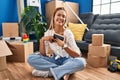 Young hispanic woman holding photo sitting on floor at new home