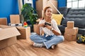 Young hispanic woman holding photo sitting on floor at new home