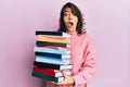 Young hispanic woman holding a pile of books afraid and shocked with surprise and amazed expression, fear and excited face Royalty Free Stock Photo