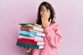 Young hispanic woman holding a pile of books covering mouth with hand, shocked and afraid for mistake Royalty Free Stock Photo