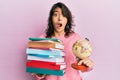 Young hispanic woman holding a pile of books and world ball afraid and shocked with surprise and amazed expression, fear and Royalty Free Stock Photo
