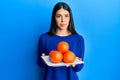 Young hispanic woman holding plate with fresh oranges relaxed with serious expression on face Royalty Free Stock Photo