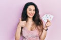 Young hispanic woman holding poker cards smiling happy and positive, thumb up doing excellent and approval sign