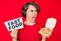 Young hispanic woman holding potato chip and fast food banner angry and mad screaming frustrated and furious, shouting with anger