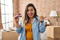 Young hispanic woman holding pregnancy test result at new home pointing thumb up to the side smiling happy with open mouth Royalty Free Stock Photo