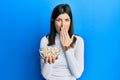 Young hispanic woman holding pumpkin seeds bowl covering mouth with hand, shocked and afraid for mistake Royalty Free Stock Photo