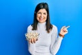 Young hispanic woman holding pumpkin seeds bowl smiling happy pointing with hand and finger to the side Royalty Free Stock Photo