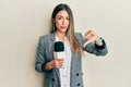 Young hispanic woman holding reporter microphone with angry face, negative sign showing dislike with thumbs down, rejection Royalty Free Stock Photo