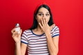 Young hispanic woman holding salt shaker covering mouth with hand, shocked and afraid for mistake Royalty Free Stock Photo