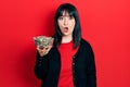 Young hispanic woman holding sunflower seeds bowl scared and amazed with open mouth for surprise, disbelief face Royalty Free Stock Photo