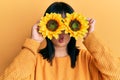 Young hispanic woman holding sunflowers over eyes making fish face with mouth and squinting eyes, crazy and comical Royalty Free Stock Photo