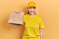 Young hispanic woman holding take away paper bag looking positive and happy standing and smiling with a confident smile showing Royalty Free Stock Photo