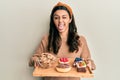 Young hispanic woman holding tray with pastries breakfast sticking tongue out happy with funny expression Royalty Free Stock Photo