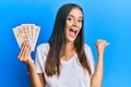 Young hispanic woman holding united kingdom pounds pointing thumb up to the side smiling happy with open mouth