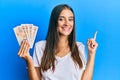 Young hispanic woman holding united kingdom pounds smiling happy pointing with hand and finger to the side