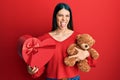 Young hispanic woman holding valentine gift sticking tongue out happy with funny expression