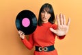 Young hispanic woman holding vinyl disc with open hand doing stop sign with serious and confident expression, defense gesture Royalty Free Stock Photo